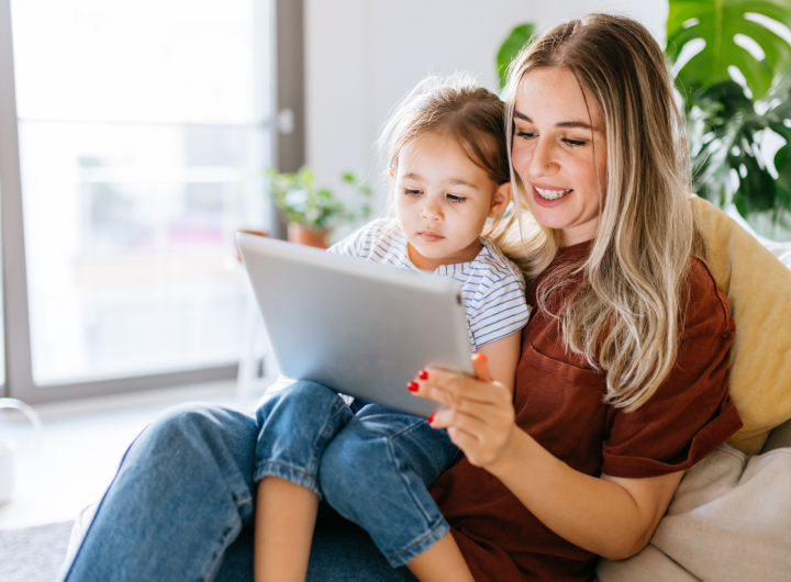 A young girl sits on her mum’s lap, watching  screens together can help with iPad tantrums